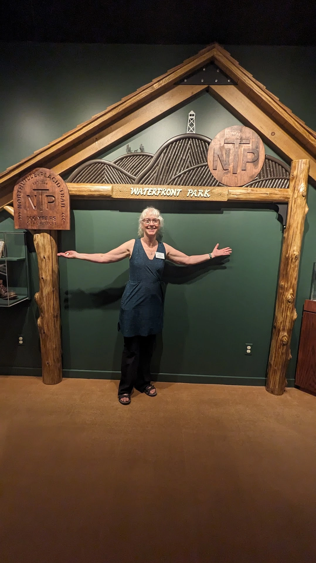 A woman smiles under a wooden arch against a green wall where plaques describing the NPT are displayed
