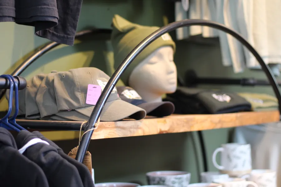 Hats adorn a mannequin head on a rough sawn shelf surrounded by other attire.