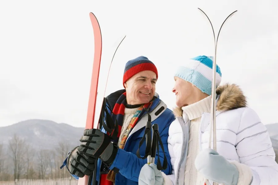 A man and woman holding skis smile at eachother
