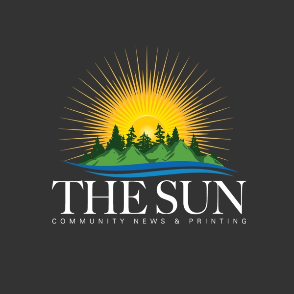 The Sun Logo of a large yellow sun, a body of water, a small green island with tall dark pine trees