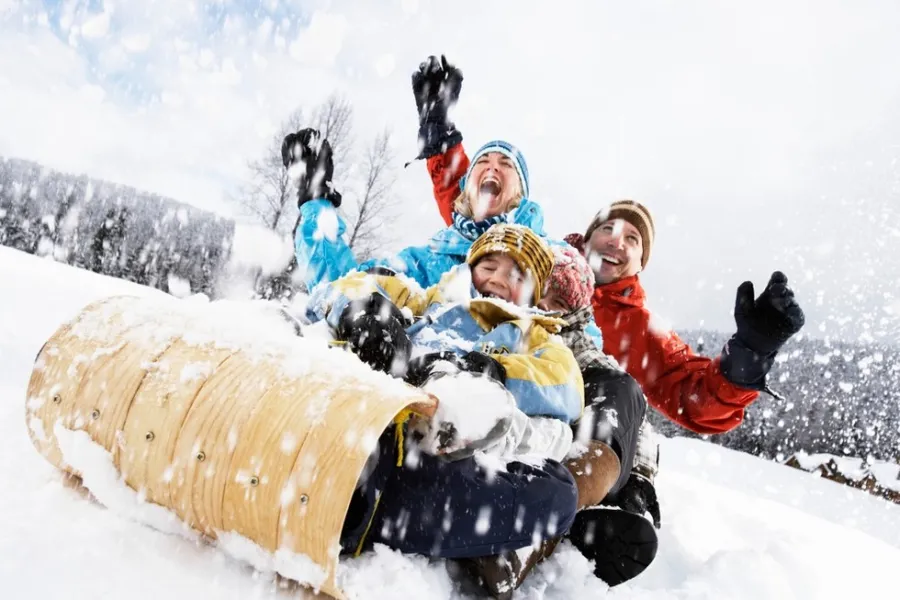 A young family laughs their way down the sledding hill on a tobogan as the snow flies around them