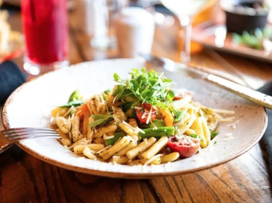 A pasta dish with cherry tomatoes, shredded parmesan and topped with microgreens.